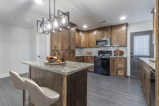 kitchen featuring dark hardwood / wood-style floors, decorative light fixtures, backsplash, a center island, and black appliances