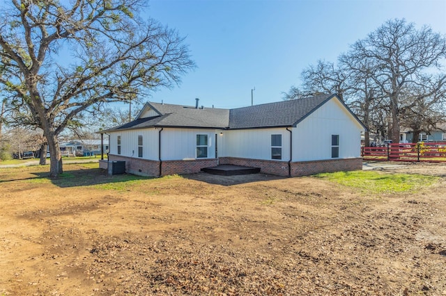 rear view of house featuring central AC unit, fence, brick siding, and roof with shingles