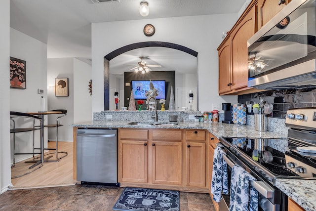 kitchen with light stone countertops, sink, ceiling fan, dark wood-type flooring, and stainless steel appliances