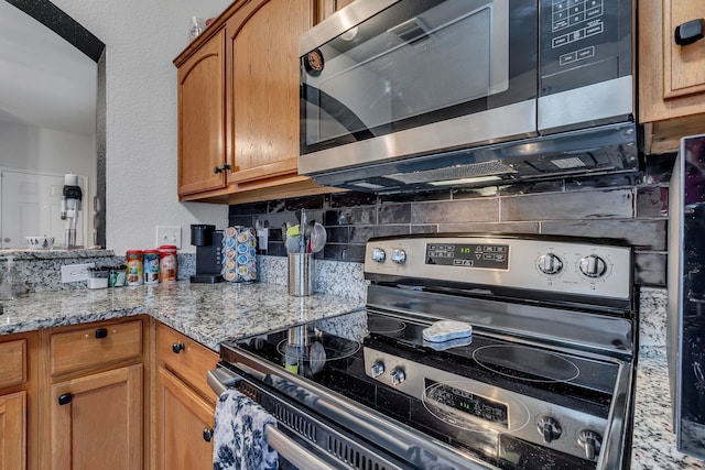 kitchen featuring decorative backsplash, light stone counters, and appliances with stainless steel finishes