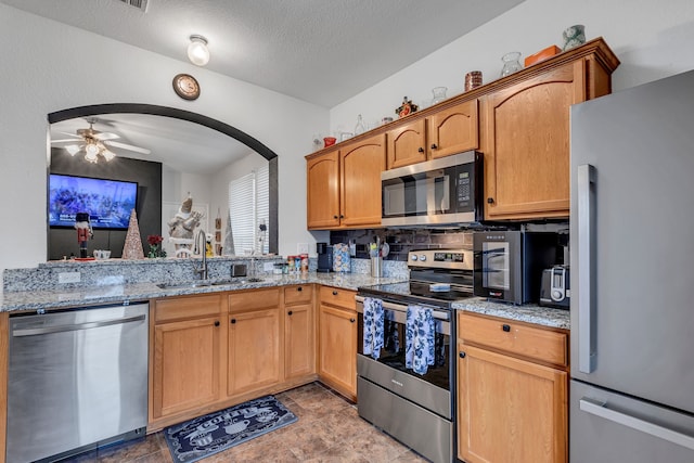 kitchen with ceiling fan, sink, light stone counters, decorative backsplash, and appliances with stainless steel finishes