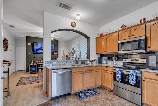 kitchen with light stone countertops, appliances with stainless steel finishes, ceiling fan, sink, and hardwood / wood-style flooring