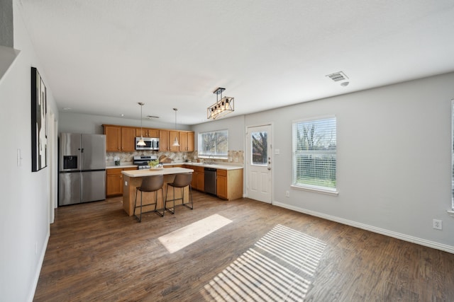 kitchen with a center island, appliances with stainless steel finishes, a kitchen breakfast bar, pendant lighting, and decorative backsplash