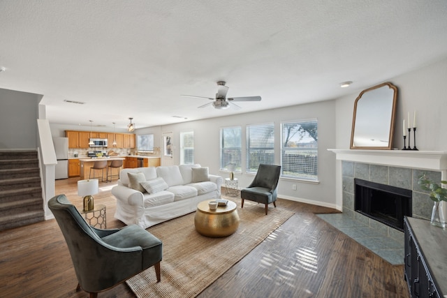 living room featuring a textured ceiling, a fireplace, dark hardwood / wood-style floors, and ceiling fan