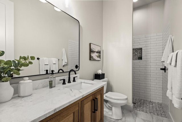 bathroom with a tile shower, vanity, and toilet