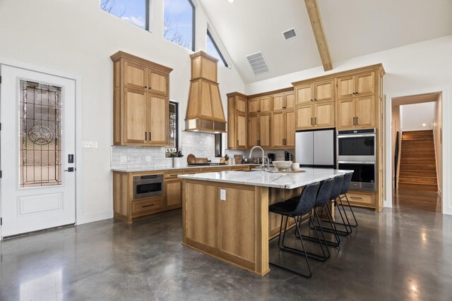 kitchen featuring high vaulted ceiling, a breakfast bar area, decorative backsplash, a center island with sink, and appliances with stainless steel finishes