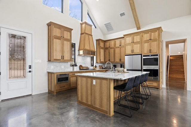 kitchen featuring appliances with stainless steel finishes, a kitchen island with sink, high vaulted ceiling, a kitchen breakfast bar, and decorative backsplash