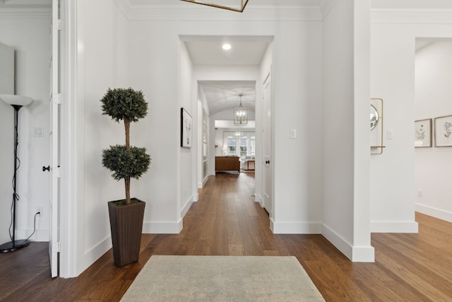 hall with ornamental molding, an inviting chandelier, and dark wood-type flooring