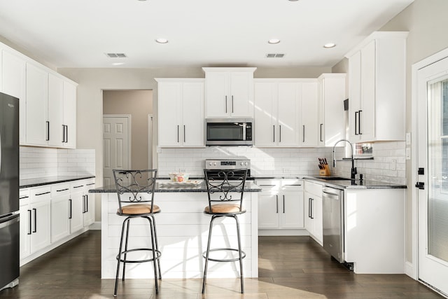 kitchen with appliances with stainless steel finishes, sink, dark wood-type flooring, white cabinetry, and a center island