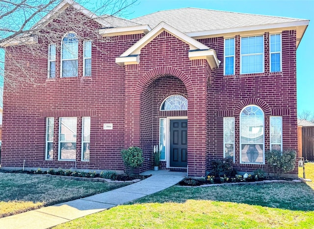 traditional-style home with brick siding, a front yard, and a shingled roof