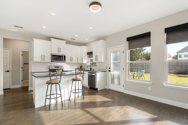 kitchen with stainless steel dishwasher, white cabinets, dark stone countertops, sink, and backsplash