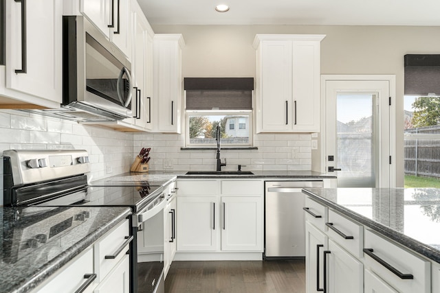 kitchen with sink, backsplash, white cabinetry, dark stone counters, and stainless steel appliances