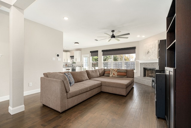 living room with a fireplace, dark wood-type flooring, and ceiling fan