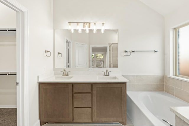 bathroom featuring a spacious closet, double vanity, a garden tub, and a sink