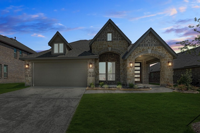 french country inspired facade with concrete driveway, stone siding, a front lawn, an attached garage, and brick siding