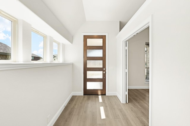 foyer entrance featuring light wood-style floors, baseboards, and vaulted ceiling