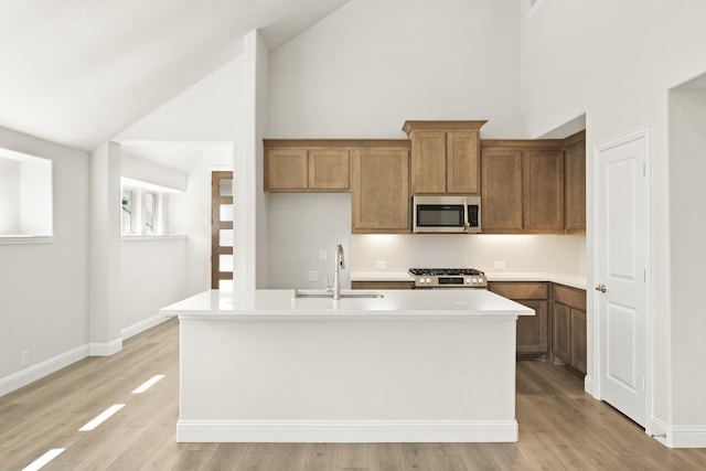 kitchen with brown cabinetry, gas range, stainless steel microwave, a sink, and backsplash