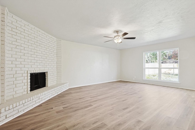 unfurnished living room featuring a brick fireplace, ceiling fan, a textured ceiling, and light hardwood / wood-style flooring