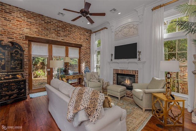 living room featuring crown molding, dark wood-type flooring, ceiling fan, a fireplace, and brick wall