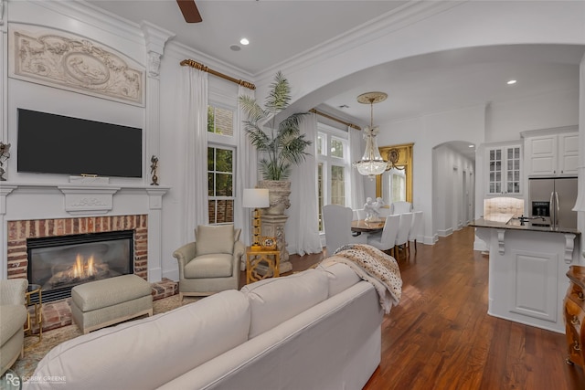 living room featuring dark hardwood / wood-style floors, a fireplace, crown molding, and an inviting chandelier