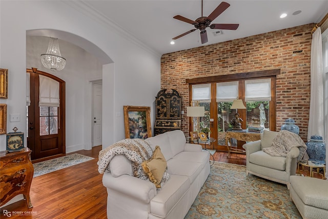 living room with crown molding, wood-type flooring, ceiling fan with notable chandelier, and brick wall