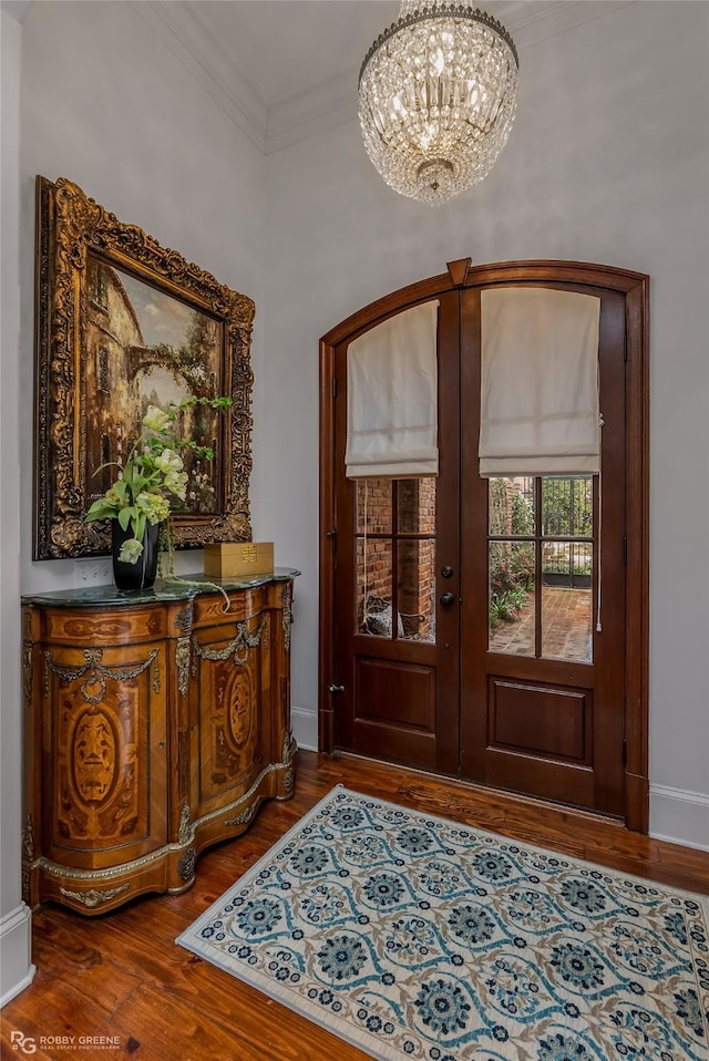 foyer entrance with ornamental molding, wood-type flooring, a notable chandelier, and french doors