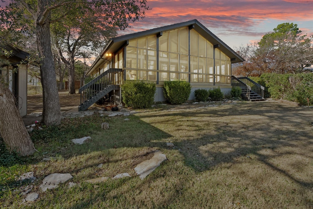 property exterior at dusk with a yard and a sunroom