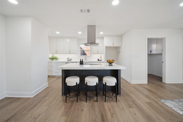 kitchen featuring a kitchen island, white cabinetry, island exhaust hood, and light hardwood / wood-style flooring