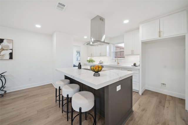 kitchen with white cabinets, sink, light hardwood / wood-style flooring, a kitchen island, and island exhaust hood