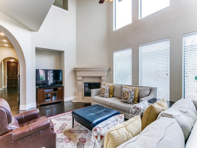 living room with ceiling fan, dark hardwood / wood-style flooring, a towering ceiling, and a fireplace