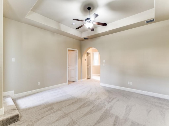 unfurnished room with a raised ceiling, light carpet, and ceiling fan