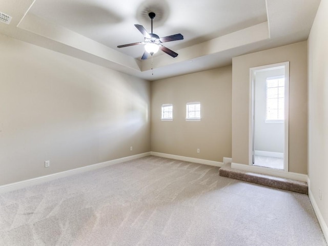 spare room featuring a raised ceiling, light colored carpet, and ceiling fan