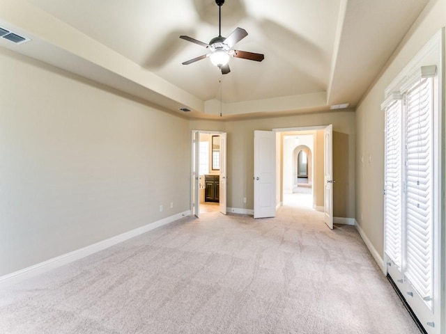 unfurnished bedroom featuring ensuite bathroom, ceiling fan, a tray ceiling, and light colored carpet