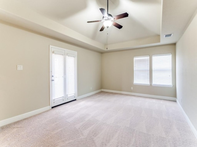 unfurnished room featuring ceiling fan, light colored carpet, and a tray ceiling