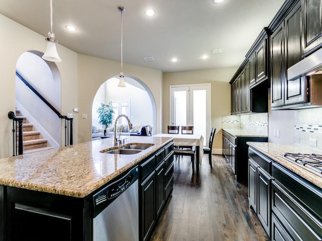 kitchen with a center island with sink, appliances with stainless steel finishes, hanging light fixtures, decorative backsplash, and sink