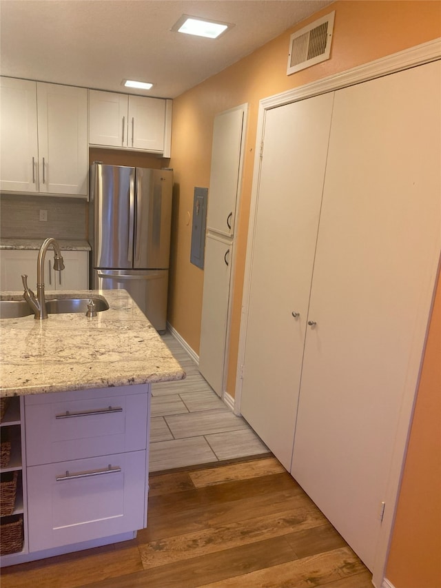 kitchen featuring stainless steel fridge, light wood-type flooring, light stone counters, sink, and white cabinets