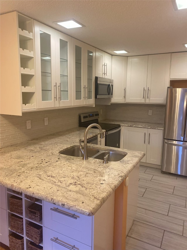 kitchen with a textured ceiling, light stone counters, white cabinetry, and stainless steel appliances