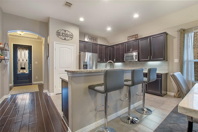 kitchen featuring dark brown cabinetry, stainless steel appliances, a kitchen breakfast bar, an island with sink, and light hardwood / wood-style floors