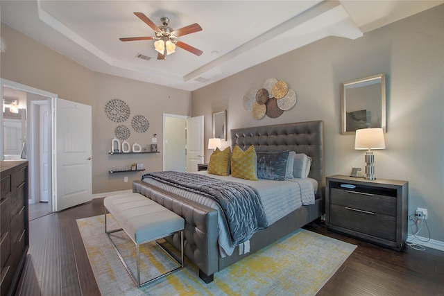 bedroom with ceiling fan, dark hardwood / wood-style floors, a raised ceiling, and connected bathroom