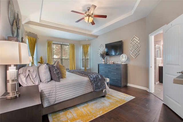 bedroom with a raised ceiling, ceiling fan, dark hardwood / wood-style flooring, and ensuite bath