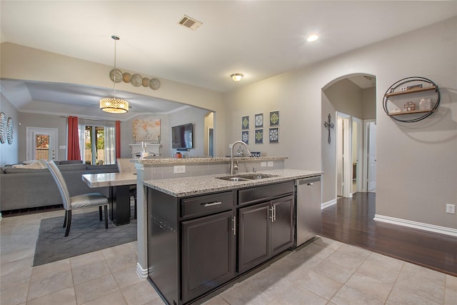 kitchen featuring sink, stainless steel dishwasher, pendant lighting, light hardwood / wood-style floors, and a kitchen island with sink