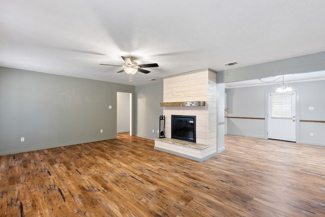 unfurnished living room featuring a large fireplace, ceiling fan with notable chandelier, and hardwood / wood-style flooring