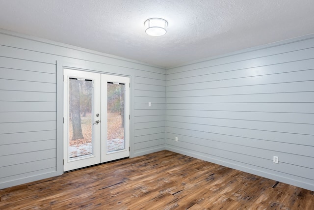 spare room featuring a textured ceiling, dark wood-type flooring, wooden walls, and french doors