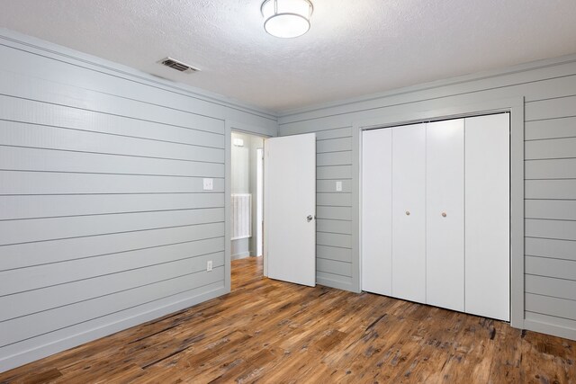 unfurnished bedroom with a textured ceiling, wood walls, dark wood-type flooring, and a closet