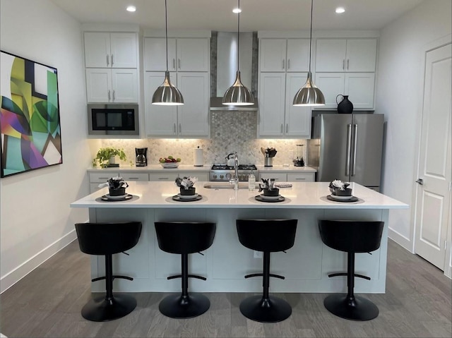 kitchen featuring a center island with sink, wall chimney exhaust hood, built in microwave, and stainless steel refrigerator