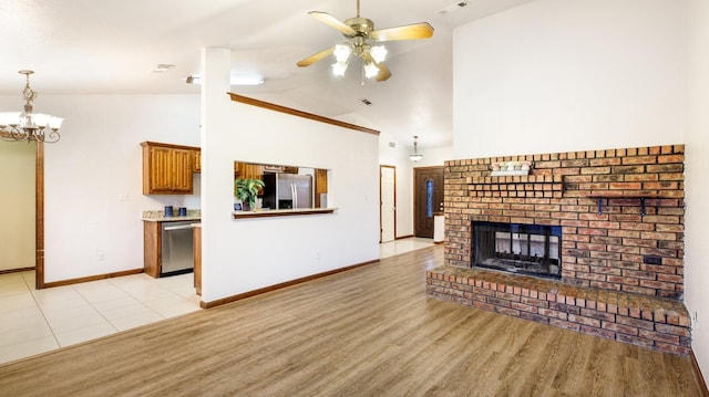 living room with high vaulted ceiling, light hardwood / wood-style floors, ceiling fan with notable chandelier, and a brick fireplace