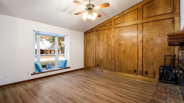 unfurnished room featuring ceiling fan, a brick fireplace, dark hardwood / wood-style floors, wood walls, and lofted ceiling