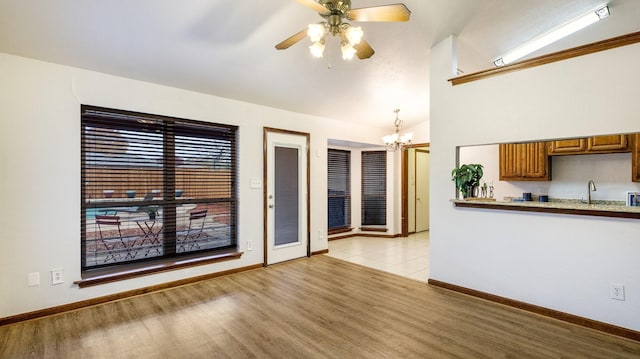 unfurnished living room with ceiling fan with notable chandelier, light wood-type flooring, lofted ceiling, and sink