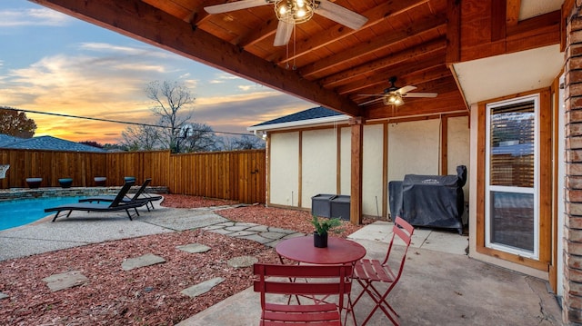 patio terrace at dusk featuring a fenced in pool, area for grilling, and ceiling fan