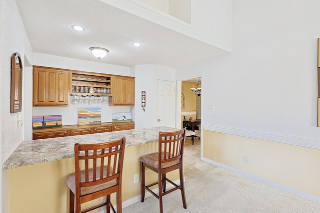 kitchen featuring an inviting chandelier, light colored carpet, a textured ceiling, a kitchen bar, and kitchen peninsula